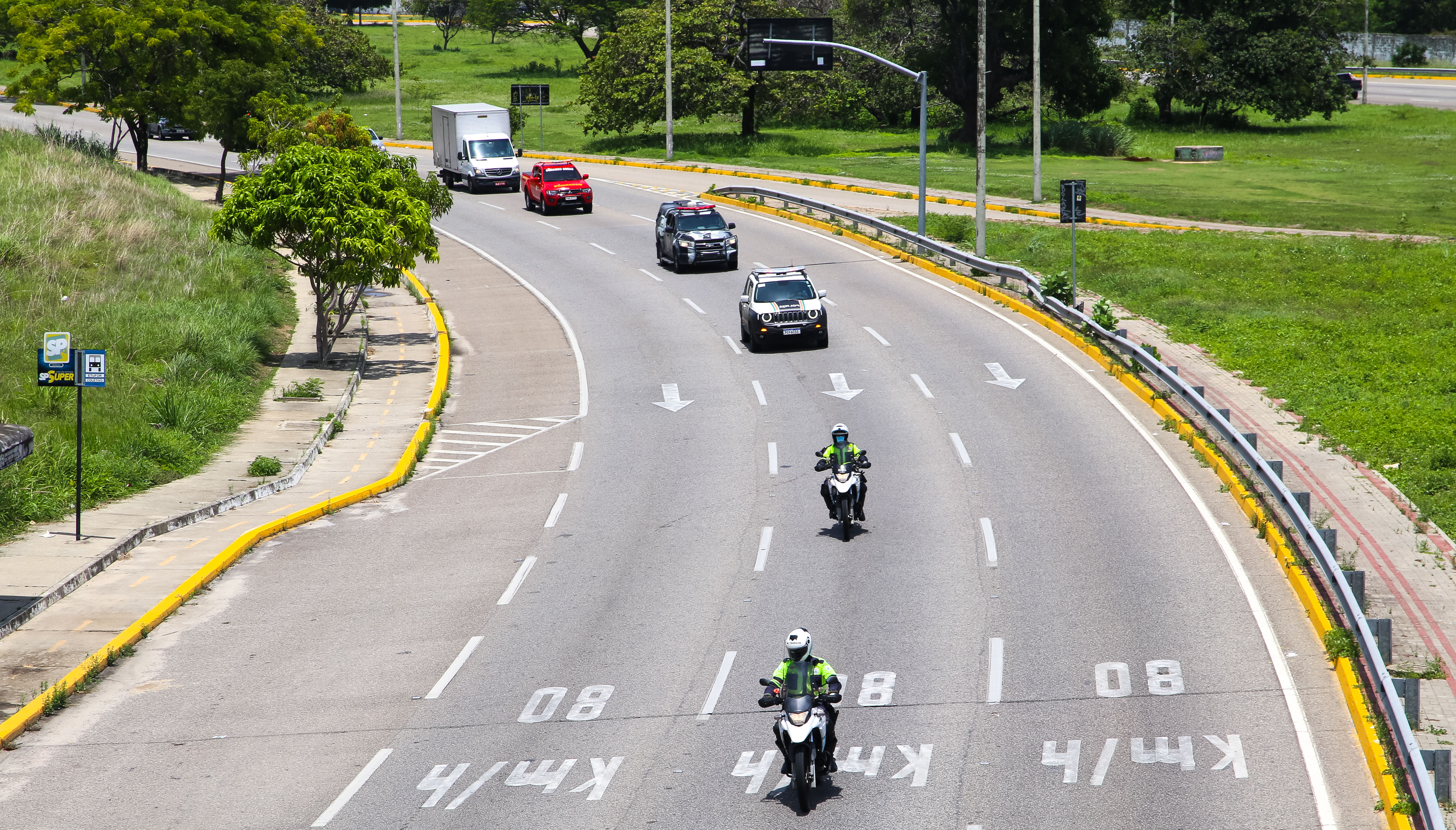 comboio de motos, carros e caminhão passa por uma avenida 